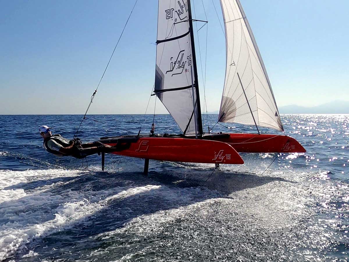 FLY15 foiling catamaran in Ferrari Red – high-performance hydrofoil sailboat, often described as a small-scale SailGP racing yacht, flying on waters with advanced carbon technology.