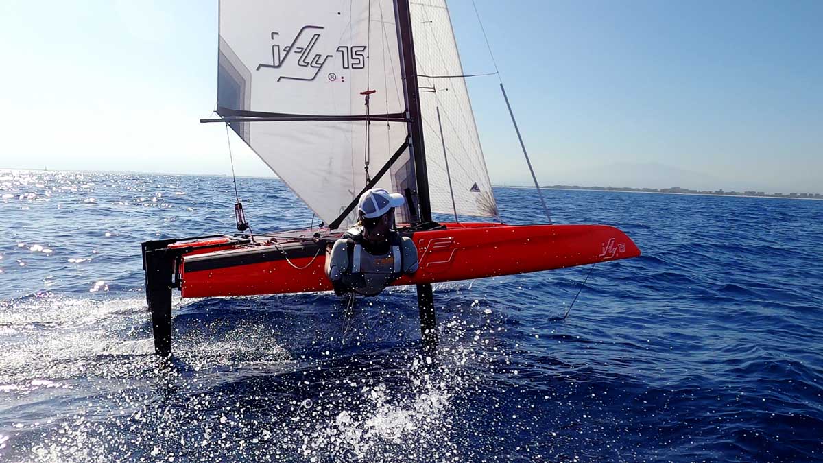 High-speed iFLY15 foiling catamaran in vibrant Ferrari Red – professional hydrofoil sailboat featuring aerospace technology for stable flight, similar to a mini SailGP racer.